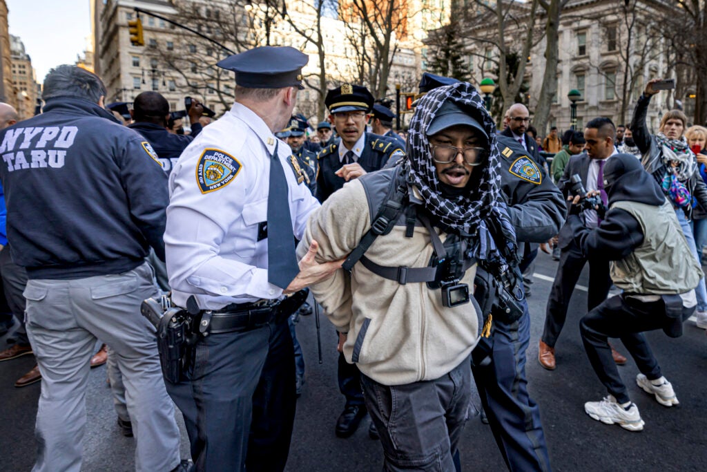 A police officer has his hand on the arm of a man being arrested but is looking behind him.