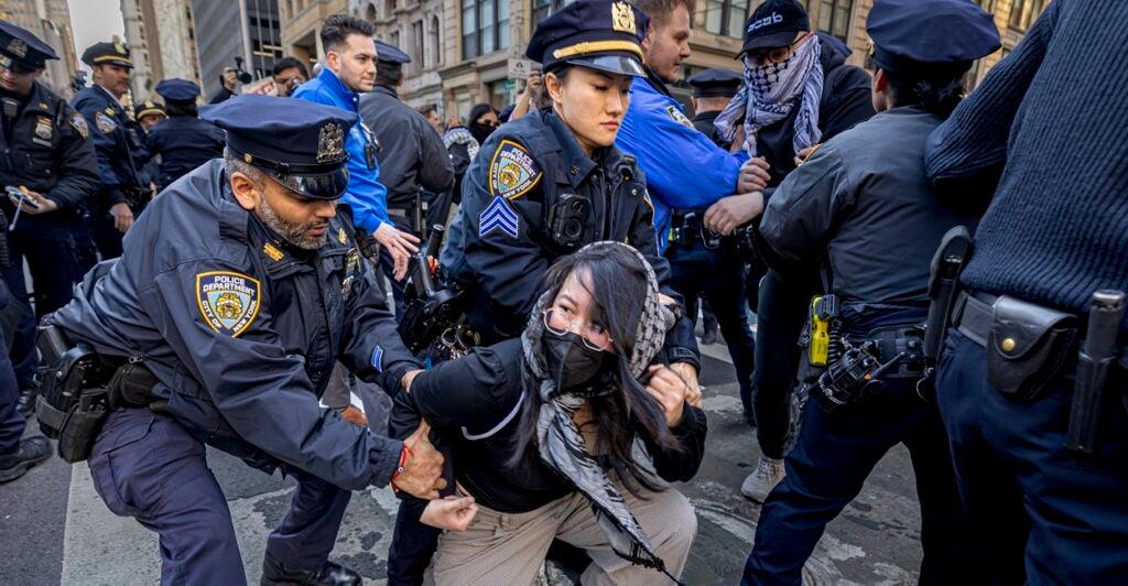 A woman is on her knees as two nearby police officers grab her.
