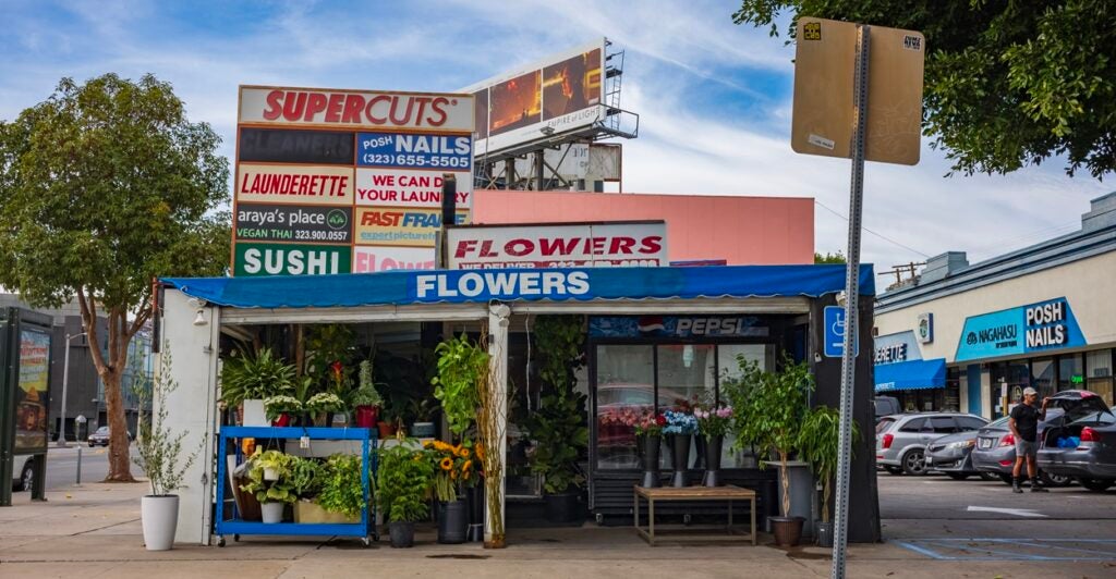 A small open-ended building has a sign that says, "Flowers" while in the background are numerous other business signs.