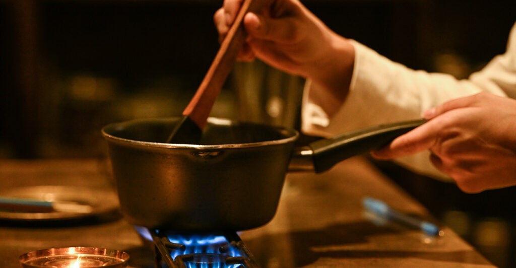 A chef stirs a pot cooking on a gas stove