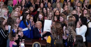 Donald Trump holds up a sign that he just signed while surrounded by females.