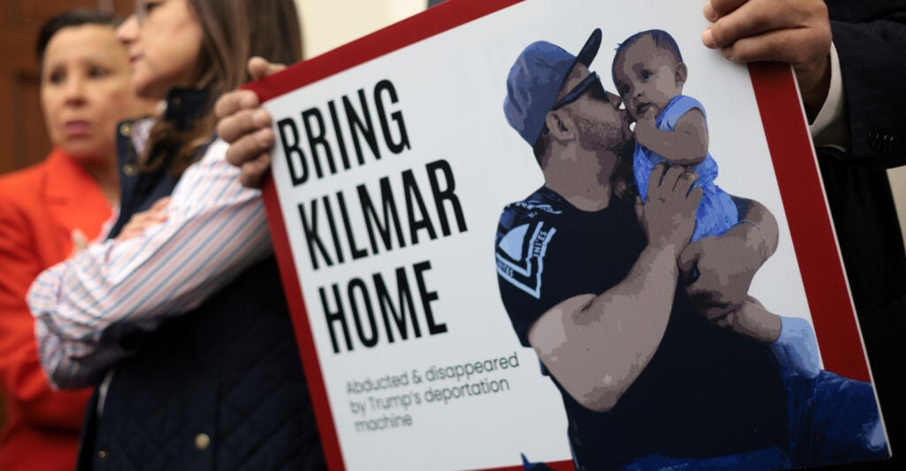 Protester holds sign reading "Bring Kilmar Home." Sign features the deported MS-13 member kissing a baby.