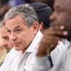 Bob Iger sits in the front row of a NBA playoff basketball game and looks straight ahead.
