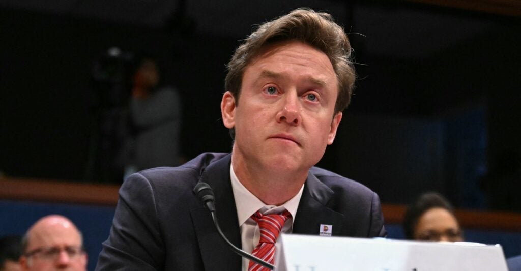 Michael Johnston sits at a desk while testifying with a microphone and name plate in front of him.