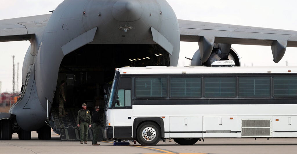 Large white bus parked next to the back of large cargo plane, its cargo door open wide.