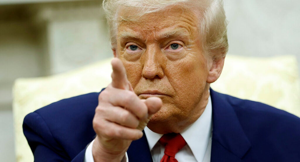 Donald Trump in a blue suit with a red tie points