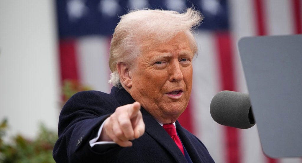 Donald Trump in a black suit points and smiles