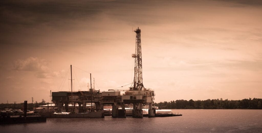 A sepia-tone image of an oil rig along the water.