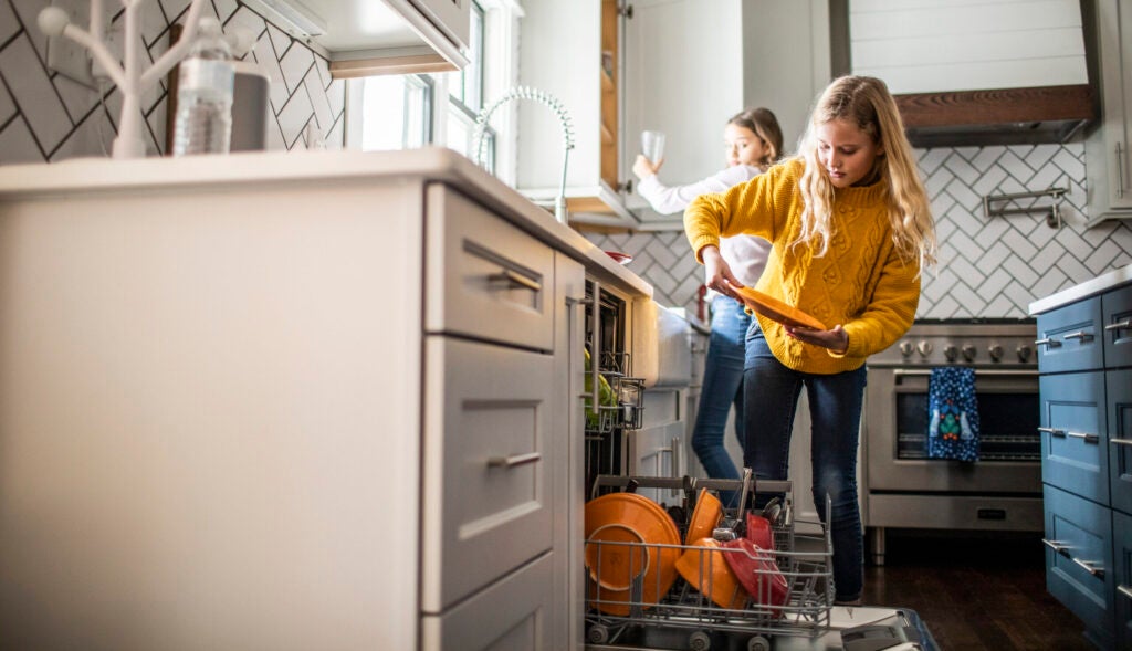 A blonde girl and brunette girl help load dishwasher.
