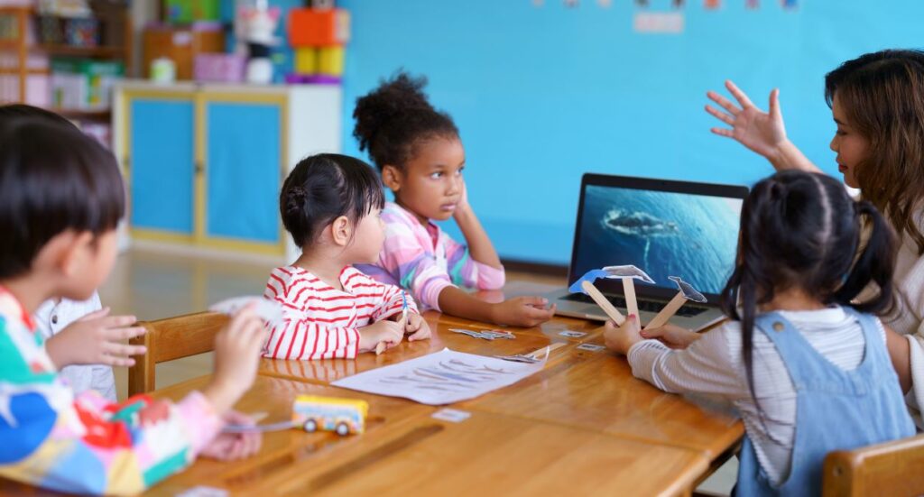 Little children in a classroom listen in rapt attention to their teacher.