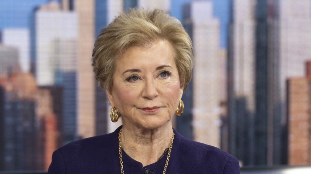 Close-up of Secretary of Education Linda McMahon, in a purple jacket, with image of New York skyline in background