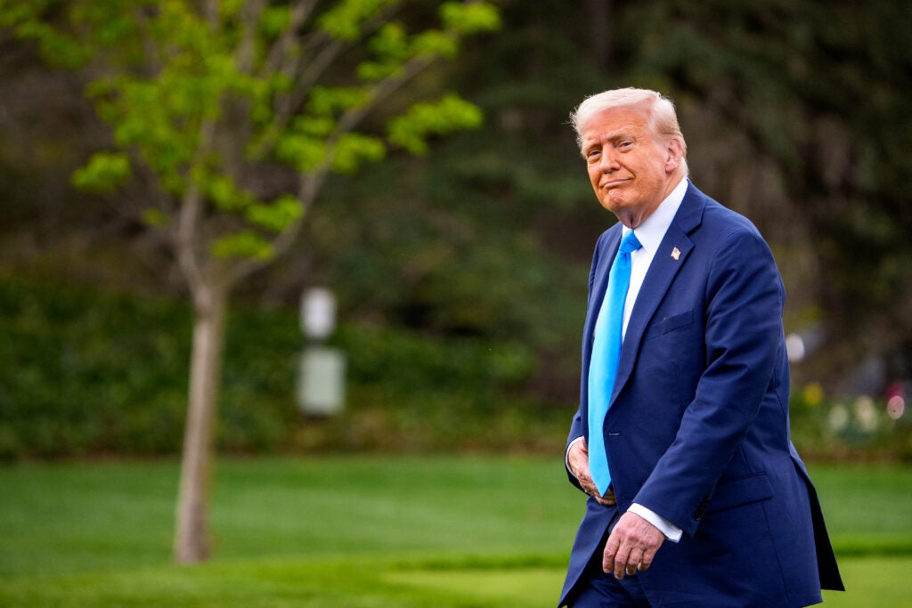 President Donald Trump in a dark blue suit and light blue tie walks outside