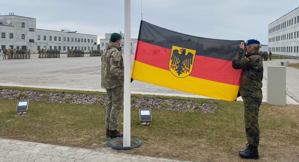 A female German soldier teams with a Lithuanian soldier in preparing to raise the German flag.