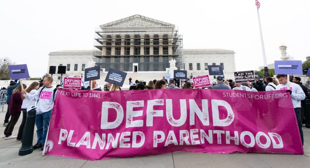 Pro-life supporters holding large "Defund Planned Parenthood" banner demonstrate in front of the Supreme Court.
