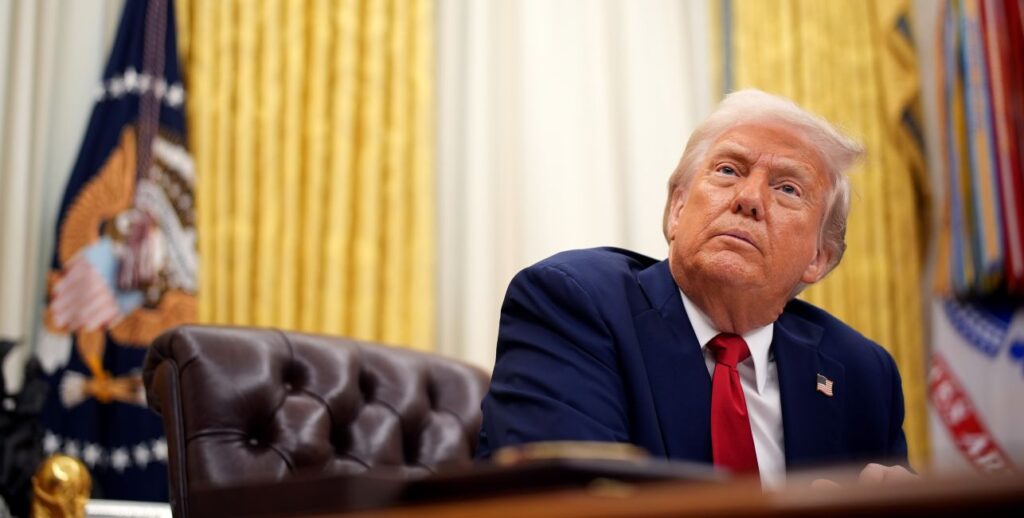 In a low-angle shot, President Donald Trump looks up from his Oval Office desk.