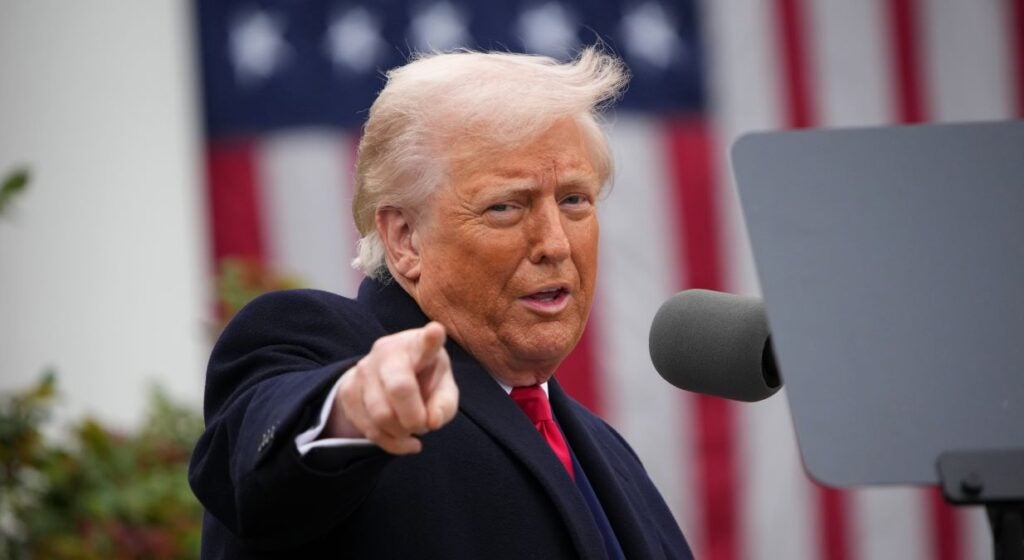 President Donald Trump pointing and speaking outside the White House in front of an American flag.