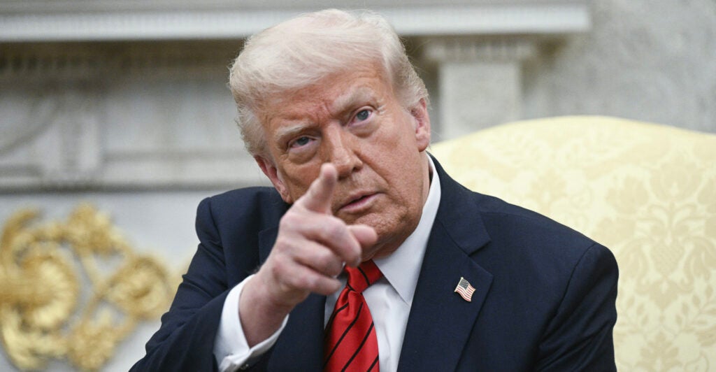 President Donald Trump points a finger while sitting in the Oval Office.
