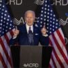 Joe Biden, fingers pointing upward, gives speech in front of two American flags.
