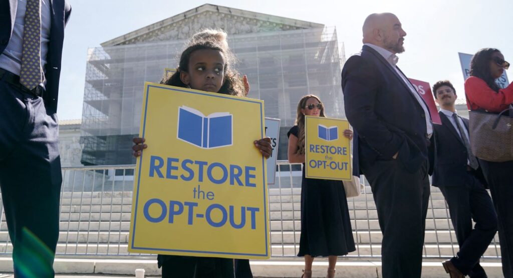 A somber-looking child holds a yellow sign with blue lettering reading "Restore the Opt-Out" with the scaffold-coffered Supreme Court behind her.