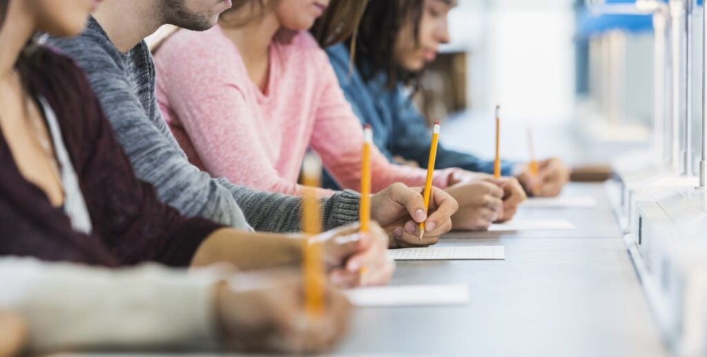 Shot down table showing five male and female high school students holding pencils take a test.