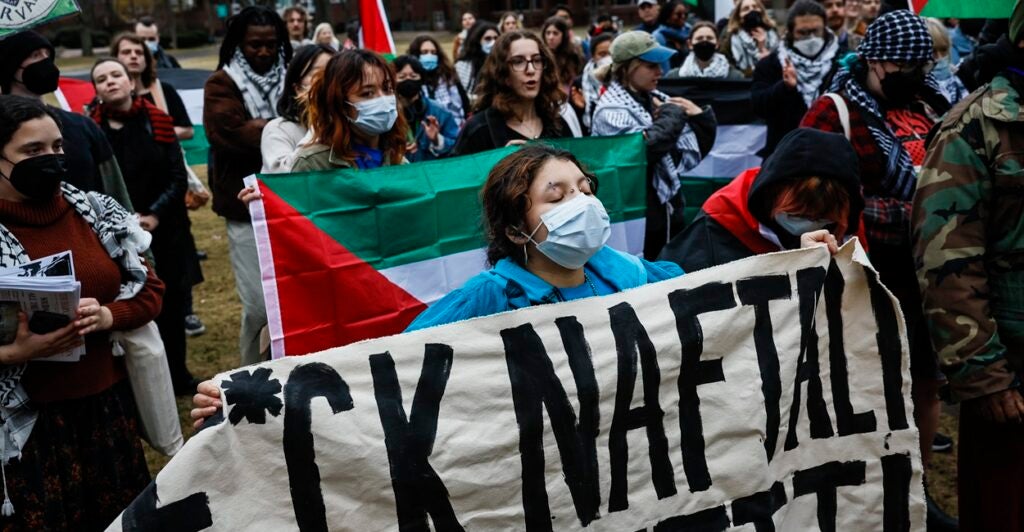 A protester at Harvard University holds an anti-Israel sign with a profanity as she marches down a street.