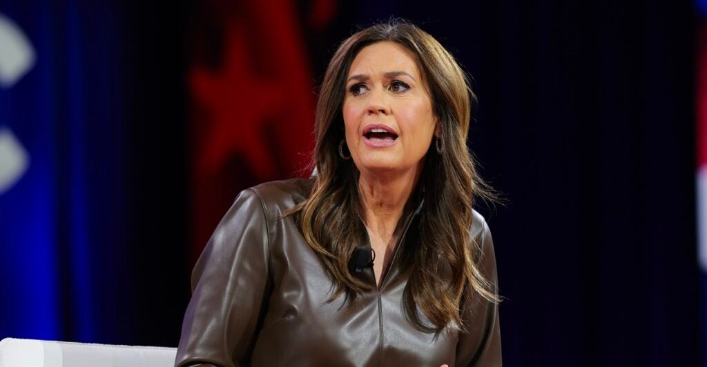 Sarah Huckabee Sanders sits down while talking at a conference with her head turned to her right.