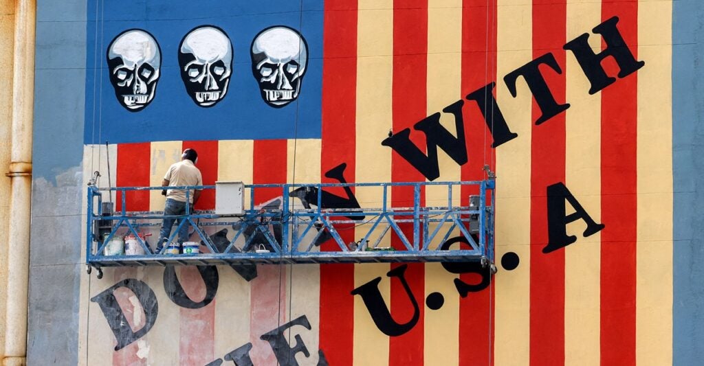 A man on a platform in Iran is putting a fresh coat of paint on an anti-America sign.