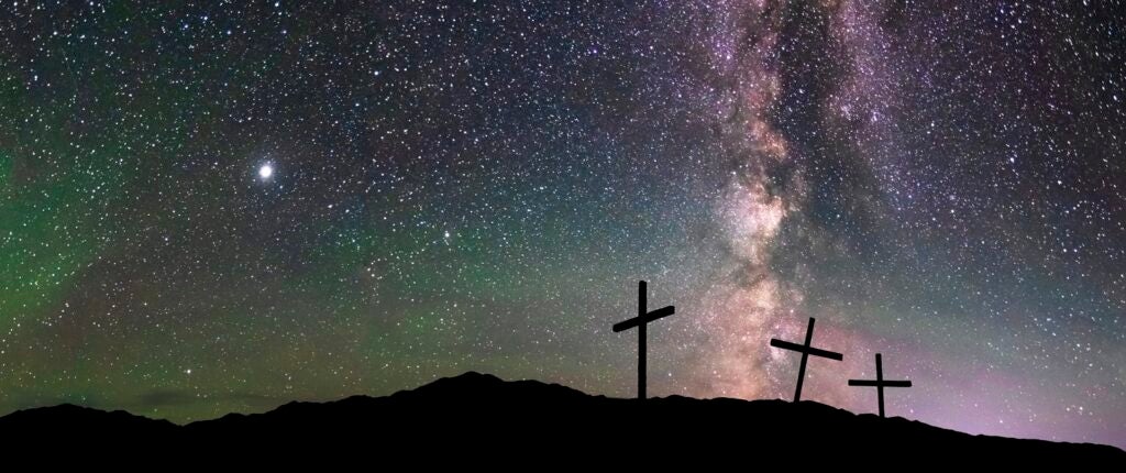 Three crosses stand on a hilltop with the stars in the background.