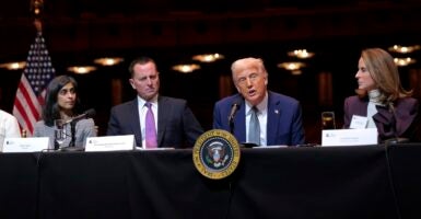 Donald Trump sits at a table and talks into a microphone during a meeting.