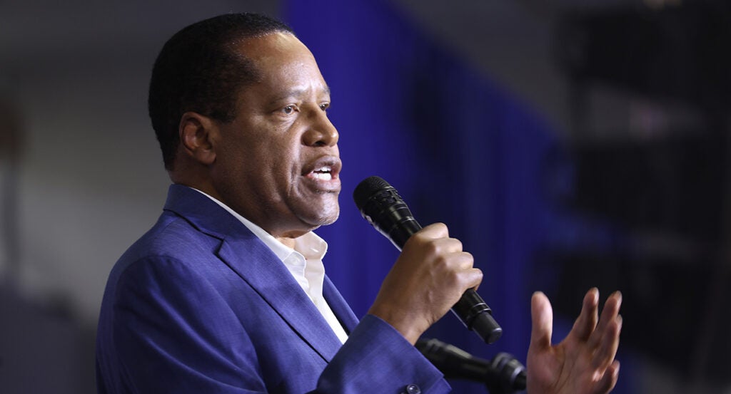 Larry Elder in a blue suit holds a microphone