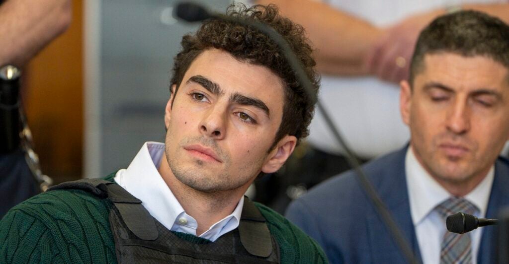 Luigi Mangione sits in court wearing a bulletproof vest as he looks to his right.