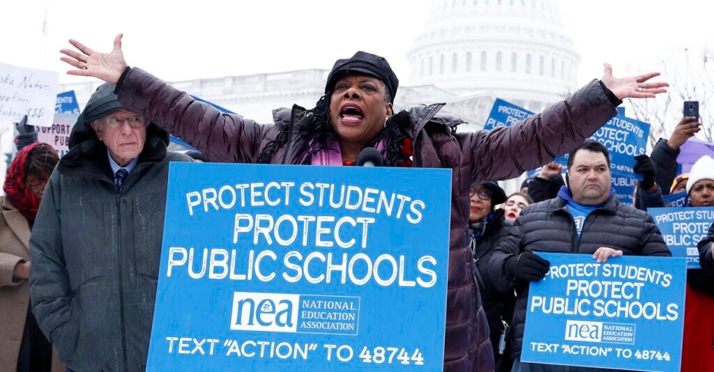 Becky Pringle stands behind a sign with both arms raised.