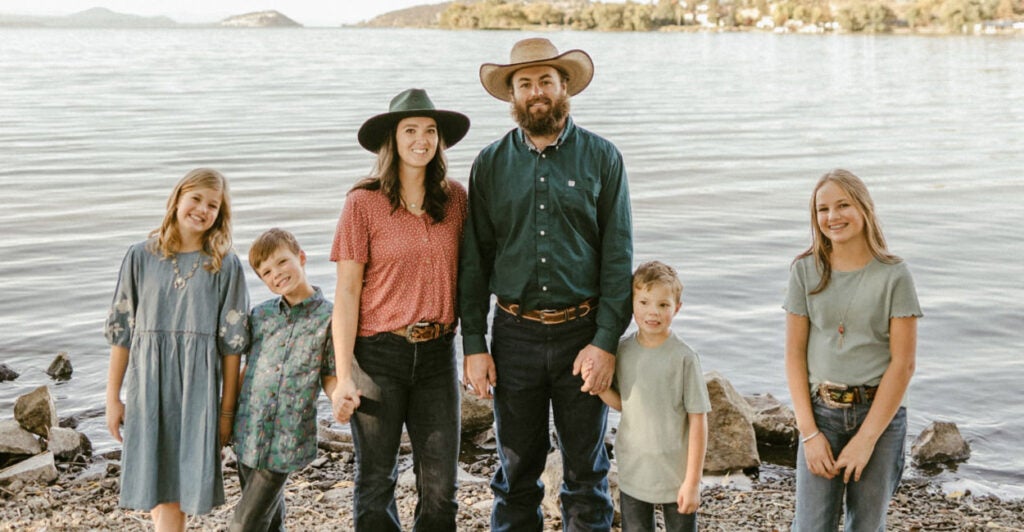 Fifth-generation farmer Rodney Cheyne with his wife in cowboy hats and their four young children standing in front of a large lake