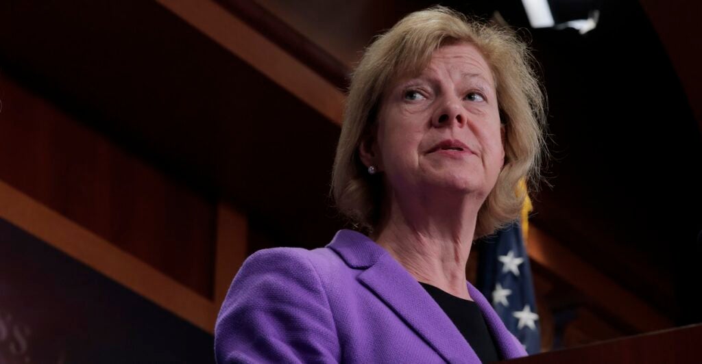 Tammy Baldwin stands at a podium and looks to her left during a news conference.