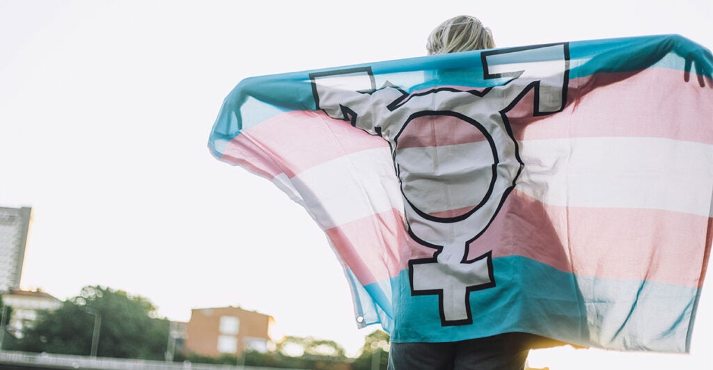 A person holds up a blue, pink, and white pro-transgender flag.