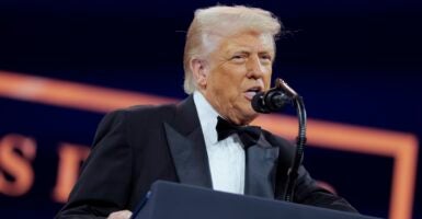 Donald Trump wears a tuxedo as he stands in front of a podium and speaks into a microphone.