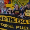 young climate activists marching and holding a banner that says end the era of fossil fuels