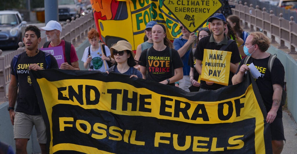 young climate activists marching and holding a banner that says end the era of fossil fuels