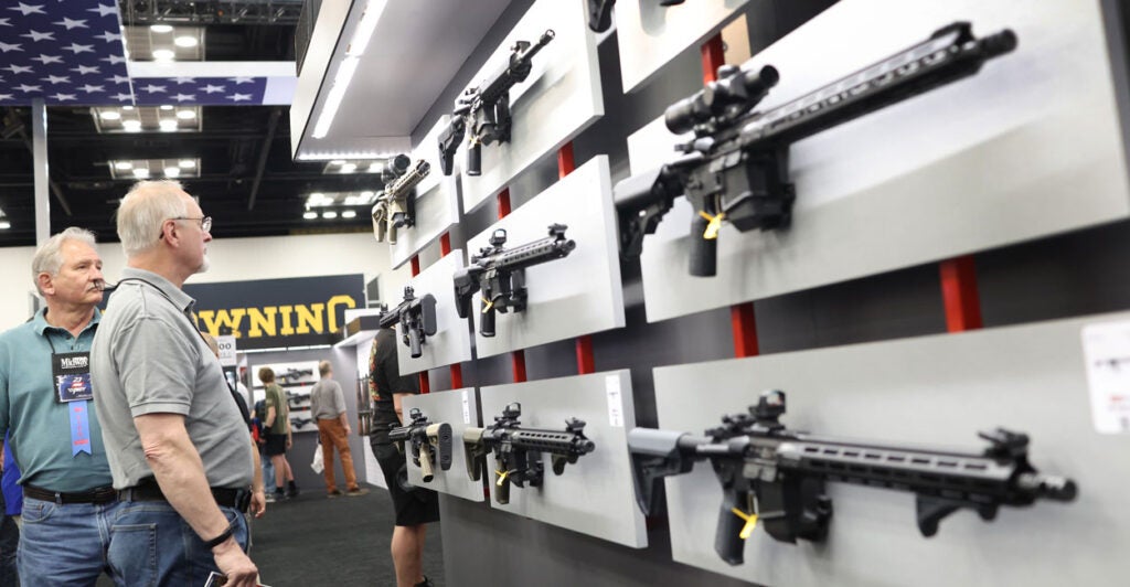 gun manufacturing Expo attendees look at several models of AR-15s displayed on a wall