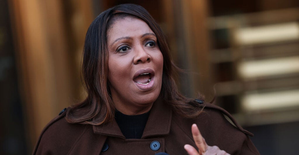 New York Attorney General Letitia James in a brown trenchcoat speaking at a podium and pointing her finger