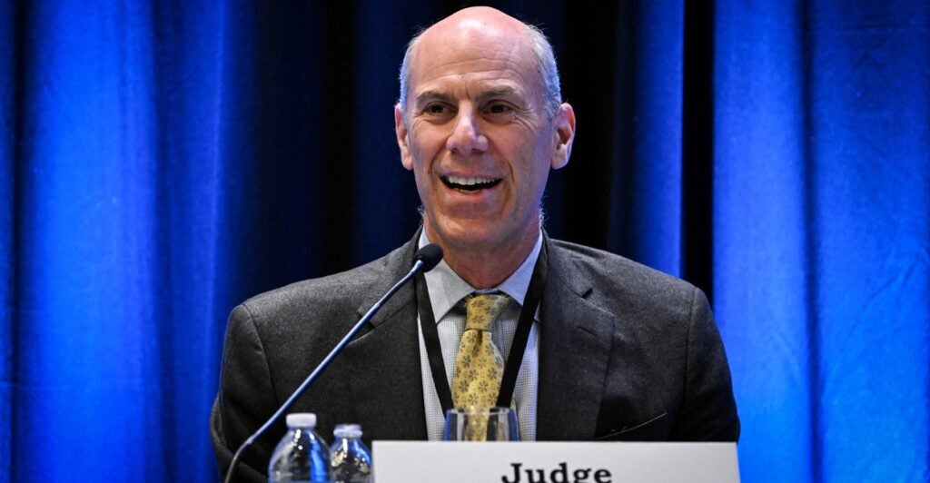 James Boasberg smiles as he sits down at a table in front of a microphone.