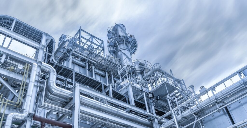 The steel pipelines of a natural gas power plant are shown with a blue sky in the background.