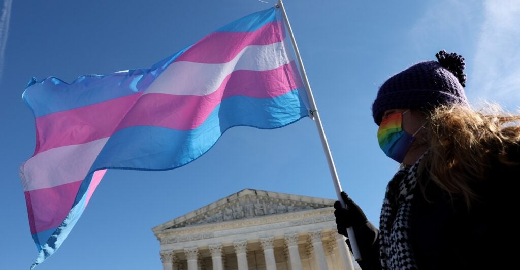 A transgender rights activist holds a transgender flag while walking.