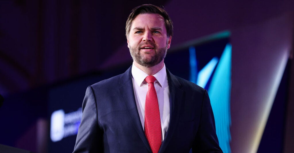 JD Vance in a blue suit and red tie smiling