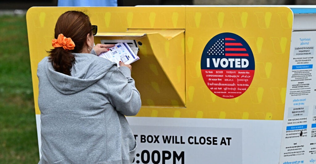 A woman inserts a voting ballot in a large ballot drop box