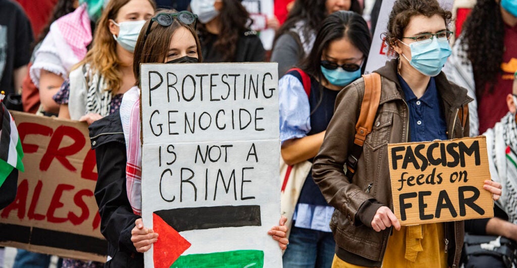 Anti-Israel protesters hold up protest signs while surrounded by a crowd of people.