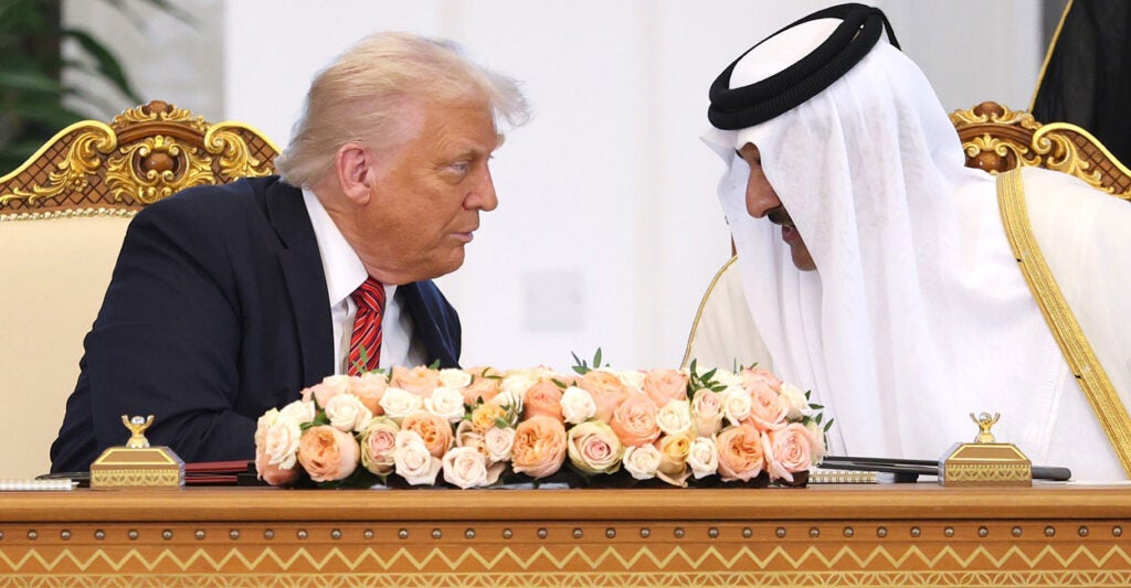 Donald Trump leans over and listens to Emir of Qatar Tamim bin Hamad al Thani as they sit at a table in Qatar.