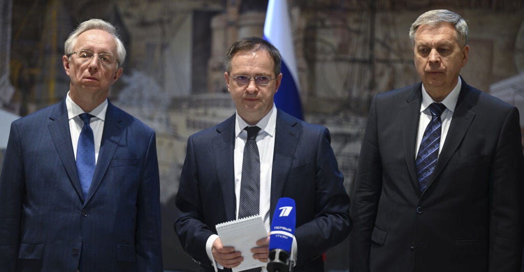 Three Russian officials stand in suits and talk to press after meeting with the Ukraine delegation.