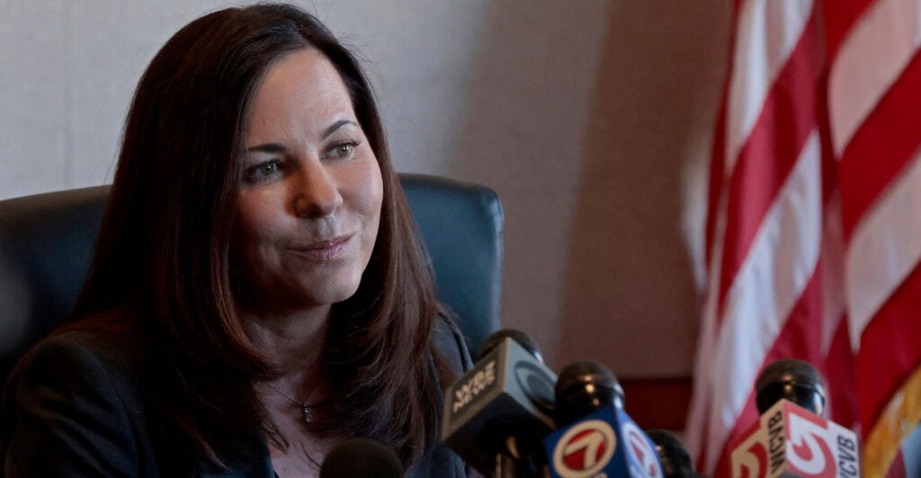 Leah Foley sits at the bench with a slight smile on her face while many microphones are before her.