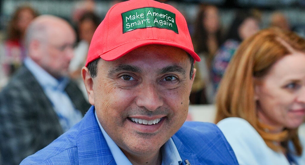 Alfredo Ortiz in a blue suit wears a Make America Smart Again hat